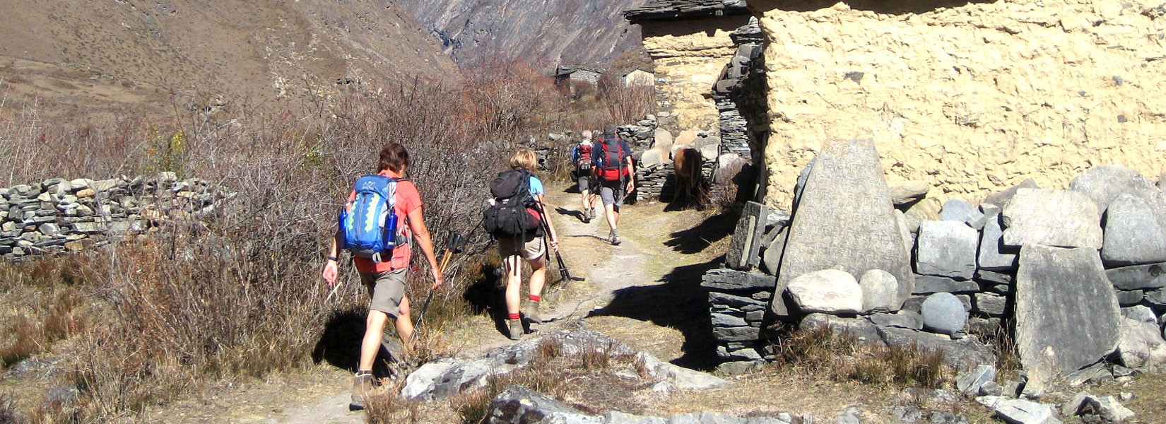 Trekkers walk by prayers wall in Tsum Valley